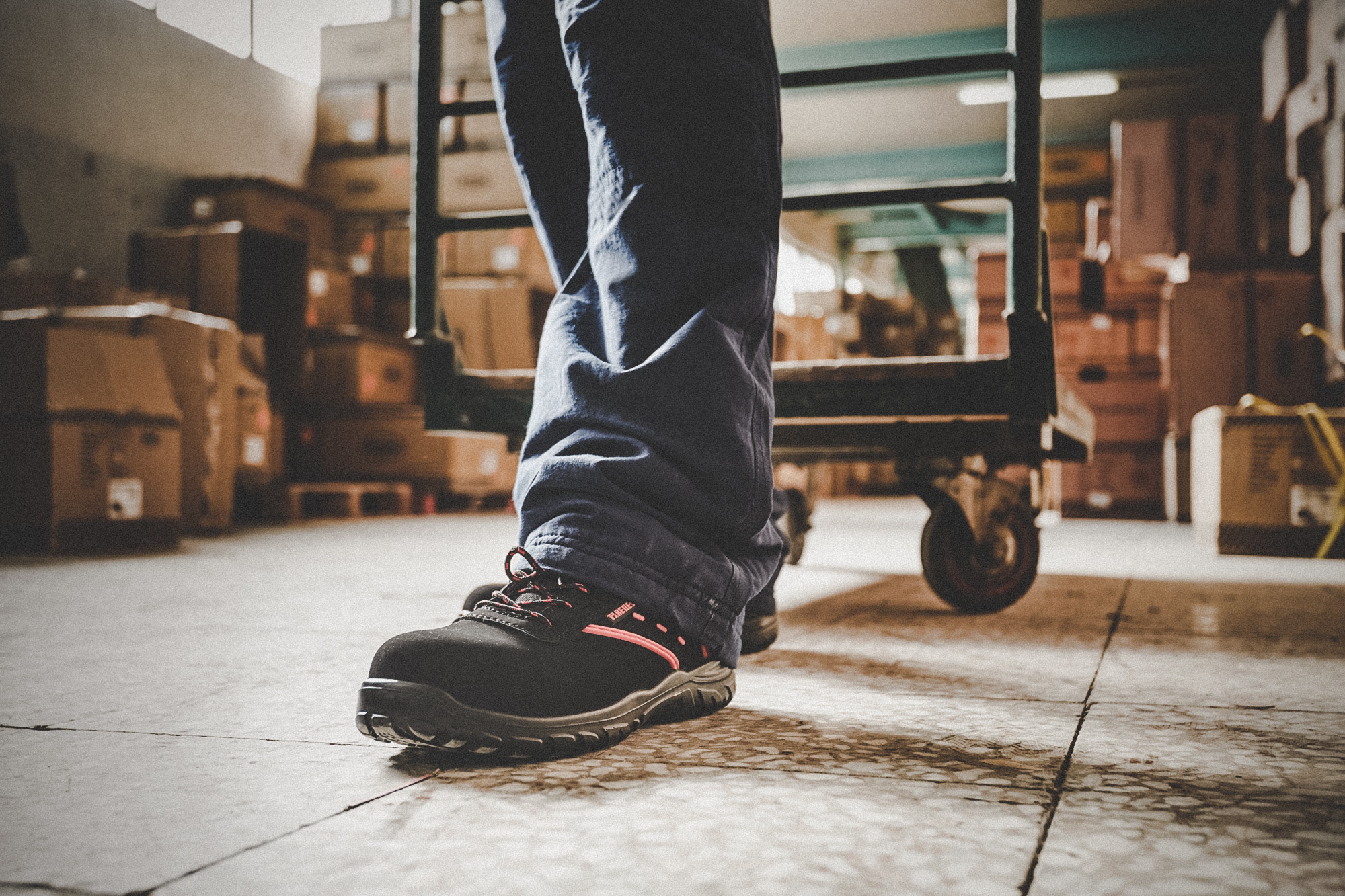 Trabajador caminando en un almacén con zapatillas de seguridad Actinio de Paredes Seguridad, mostrando la suela antideslizante y el uso en entorno industrial.